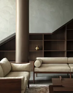 A modern living room with a textured wooden column, upholstered fabric seating, and dark wood shelves against a textured wall