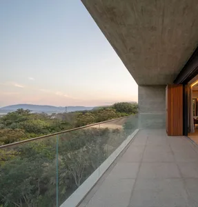 A modern residential balcony featuring concrete structure and glass railings overlooking a forested landscape.