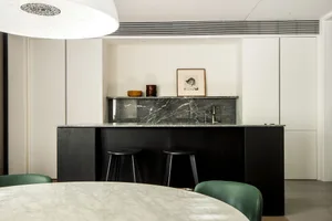 A minimalist kitchen interior with a marble countertop and black bar stools.
