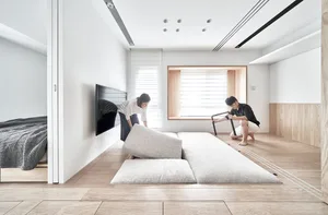 A minimalist living room with white tiles, a sofa, a TV, and a bed.