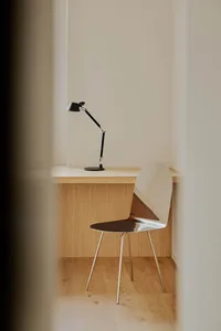 A modern home office featuring a sleek, minimalist desk made of light wood with a black adjustable desk lamp and a modern met