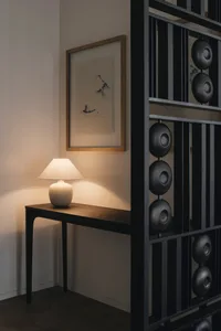 A modern living room featuring a wooden side table with a white lamp, a framed painting on the wall, and a black and metal sc