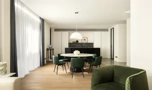 Modern minimalist kitchen with a round marble dining table, green leather chairs, and white pendant light.