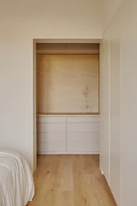 A minimalist bedroom storage unit featuring neutral-toned drawers and a vase with a dried plant against a natural wood floor 