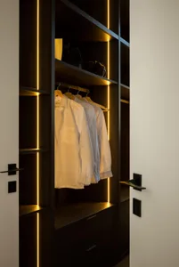 Modern wardrobe with white shirts on hangers and illuminated wooden structure with vertical lines, minimalist design.