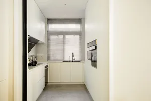 A modern white kitchen with white cabinets, a white countertop, and a large window.