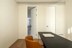A modern office space featuring minimalist design with white walls, wooden desk, and leather chair.