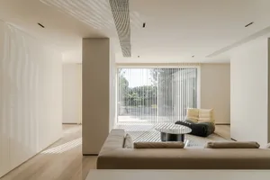 A modern living room with neutral tones and a minimalist design, featuring a large window with vertical blinds and a view of 