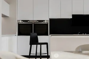A modern, minimalist kitchen with white high-gloss cabinets and a black backsplash.