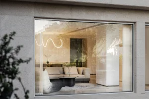 Modern living room with glass windows and beige sofa, natural light, and greenery outside.