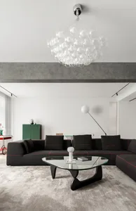 Modern living room with a concrete ceiling beam, a black sectional sofa, and a glass coffee table.