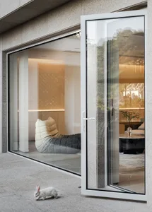 A modern minimalist living room with a glass door and a cozy seating area.