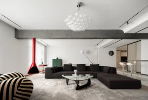 A modern living room featuring a concrete beam, a glass fireplace, and black sofas with red accents on a plush carpet.