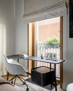 A minimalist home office featuring a sleek black desk, white ergonomic chair, and a window overlooking a red-brick building w