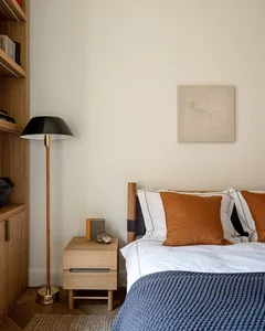 A modern minimalist bedroom with wooden furniture, a floor lamp, and a bed with white sheets and orange pillows.
