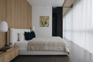 A modern bedroom with a wooden headboard, white bedding, and abstract art on the wall.