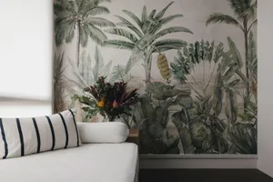 A cozy living space with a white sofa, striped pillows, and a floral arrangement in front of a botanical-themed wallpaper wal