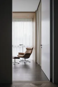 Modern living room with minimalist design, featuring a tan leather swivel chair with matching ottoman on wooden flooring, lar