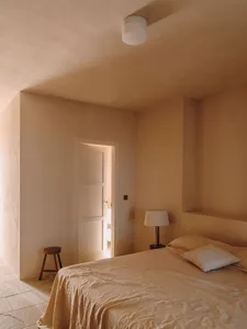 A minimalist bedroom with beige plaster walls and a simple bed setup.