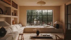 A minimalist living room featuring concrete walls, a large window overlooking an olive grove, and a wooden coffee table with 