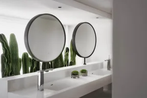 Modern minimalist bathroom with concrete countertop, white sinks, chrome faucets, and round mirrors.