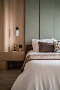 Modern minimalist bedroom featuring a bed with white bedding and brown pillows, set against a wooden cabinet and green wall p