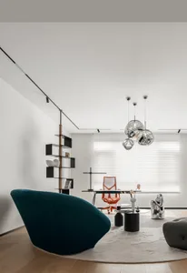 A minimalist home office featuring a sleek, metallic desk and orange chair, surrounded by contemporary decor and a large wind