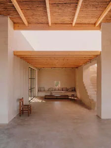 A minimalist living room with concrete flooring, wooden beams, and beige seating arrangement.
