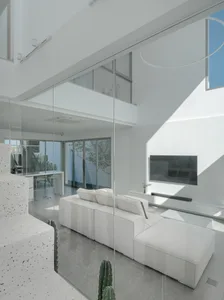 A modern, minimalist living room with glass walls and a white, modular sofa.