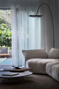 Modern minimalist living room featuring a fabric sofa, glass lamp, and sheer curtains.