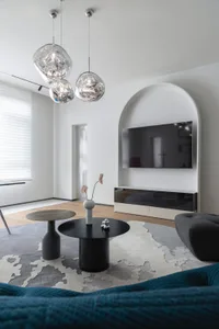 A modern minimalist living room featuring metal pendant lights, wooden flooring, and fabric seating.