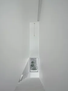 White terrazzo staircase with minimalist design leading to a window with a view of a stone garden.