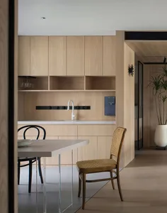 A modern, minimalist kitchen featuring wood cabinetry and furniture.