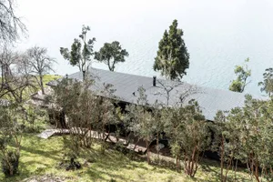 A modern beach-front house with a metal and wood exterior, featuring glass windows looking out to the ocean.