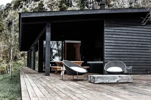 A modern black cabin with a wooden deck and white cushioned chairs.