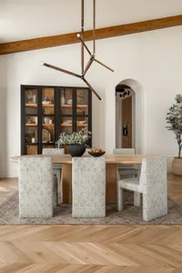 Modern dining room featuring a wooden table and upholstered chairs with a chandelier and plant.