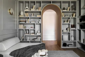A modern minimalist bedroom with shelves filled with books and decorative items, featuring a bed with white and grey bedding,