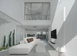 A minimalist living room with white concrete walls, a white sectional sofa, and a concrete coffee table.