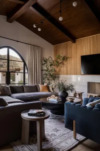 A modern residential living room featuring a sectional sofa, round coffee table, and marble fireplace with wood accents.