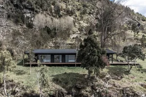 A rustic residential building with large glass windows sits on a green hillside.