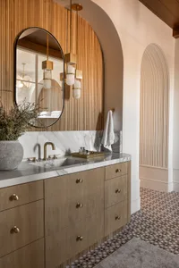 Modern minimalist bathroom featuring a wood panel wall, marble countertop, and gold fixtures.