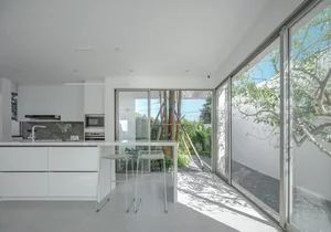 Modern, minimalist residential kitchen with large glass windows and a white color palette.