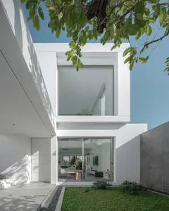 Modern minimalist white concrete house with large glass windows and greenery.