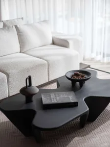 A modern living room with a white textured fabric sofa and a uniquely shaped black coffee table.