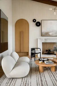 A modern living room featuring a cozy curved sofa, a round wooden coffee table, a black chair, a marble fireplace, and a stri