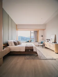 A modern minimalist bedroom featuring a bed with white bedding and decorative pillows, a wooden floor, and a view of the moun