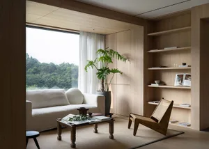 A modern minimalist living room with a white sofa, wooden coffee table, and a large green plant in a wooden pot.