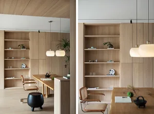 A minimalist office space featuring wooden walls and shelves with books and decorative items, illuminated by hanging lamps.