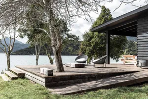 Modern minimalist patio with wooden deck, white cushions, and natural surroundings.