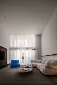A modern minimalist living room with a large floor-to-ceiling window covered by sheer curtains, featuring a blue bean bag cha